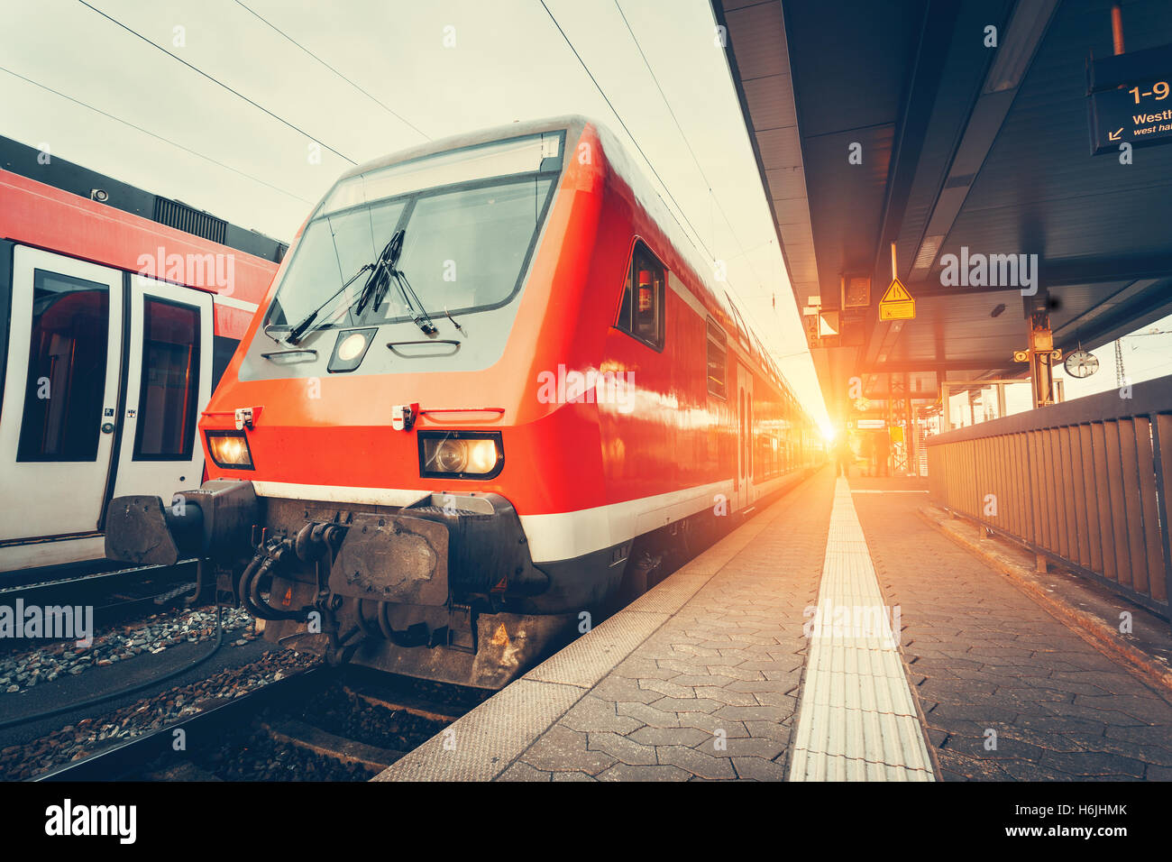 Modern high speed red commuter train at colorful sunset. Beautiful railway station. Railroad with vintage toning. Train at railw Stock Photo