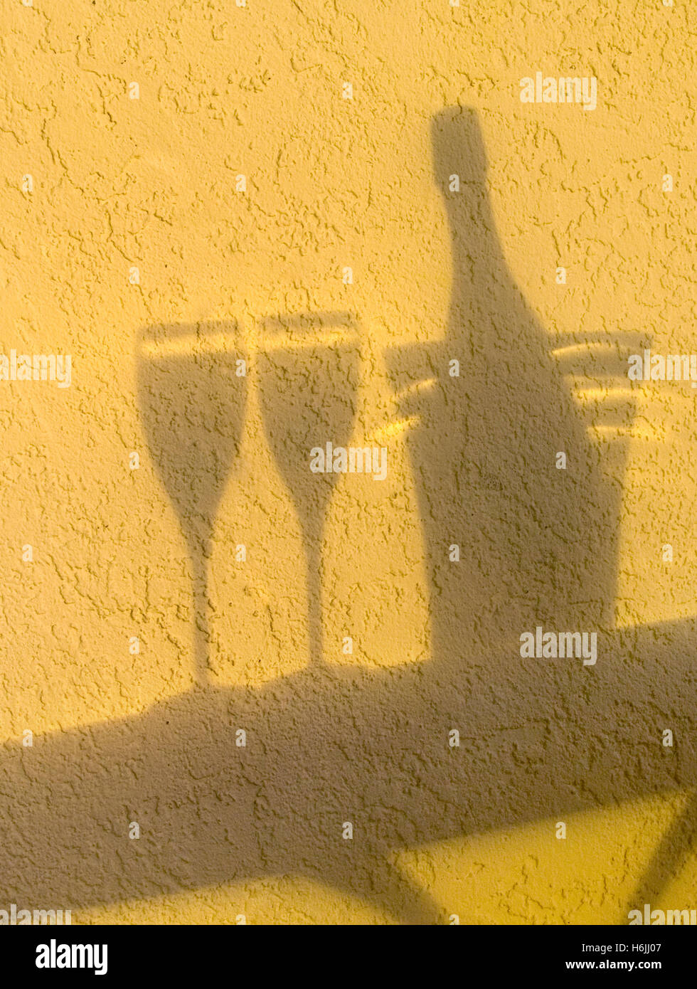 Shadow silhouette of sparkling Champagne wine bottle, ice bucket and two glasses on alfresco terrace table at sunset Stock Photo