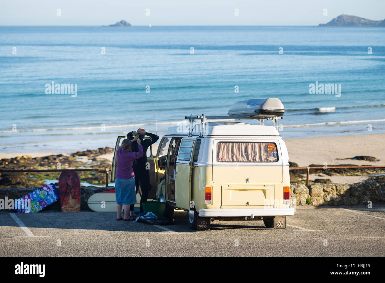 Surfers at a vintage Volkswagen camping bus preparing a wetsuit for a morning surf at Sennen Cove at early morning, Cornwall, UK Stock Photo