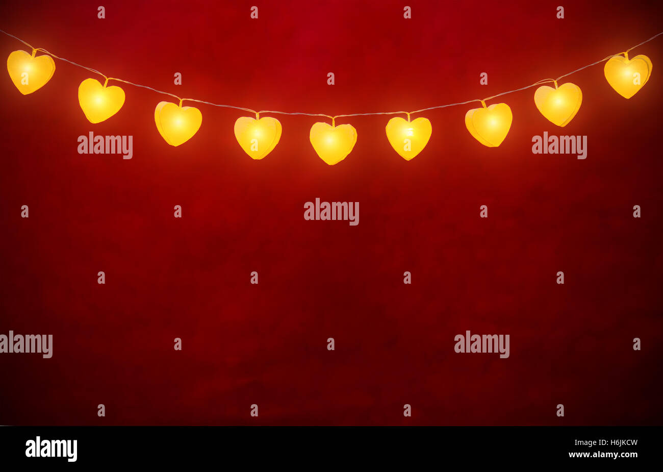 Hanging lights in heart shapes on rope with abstract empty red background Stock Photo