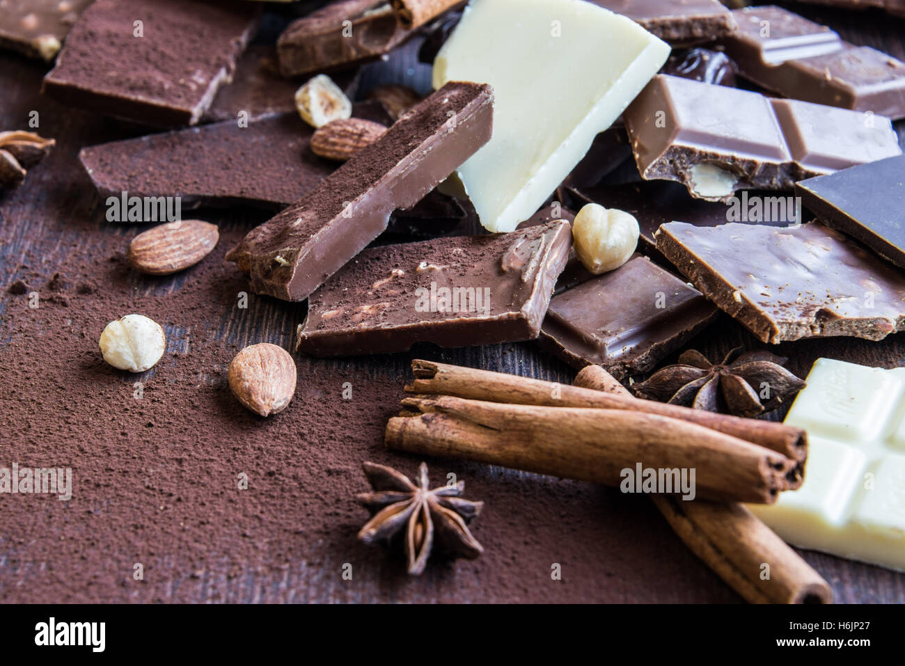 Close up of a heap of various chocolate pieces over dark wood background. Dark, milk, white and nuts chocolate bars. Cinnamon, s Stock Photo