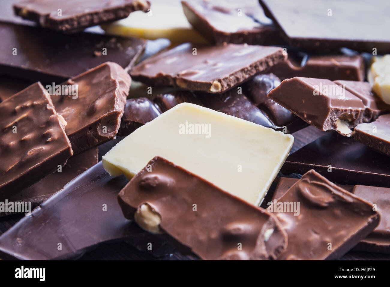 Close up of a heap of various chocolate pieces over dark wood background. Dark, milk, white and nuts chocolate bars. Stock Photo