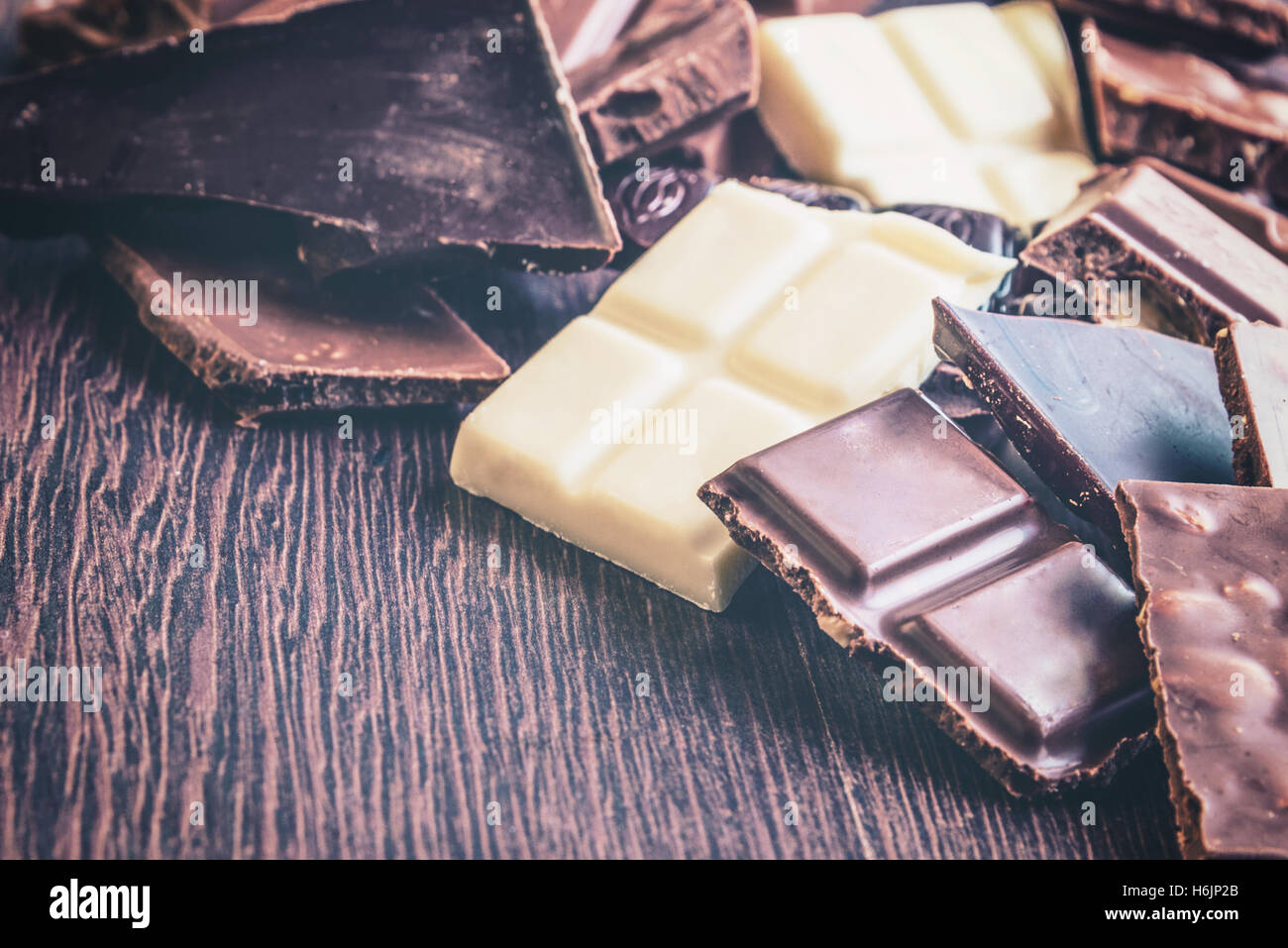 Close up of a heap of various chocolate pieces over dark wood background. Dark, milk, white and nuts chocolate bars. Copy space. Stock Photo