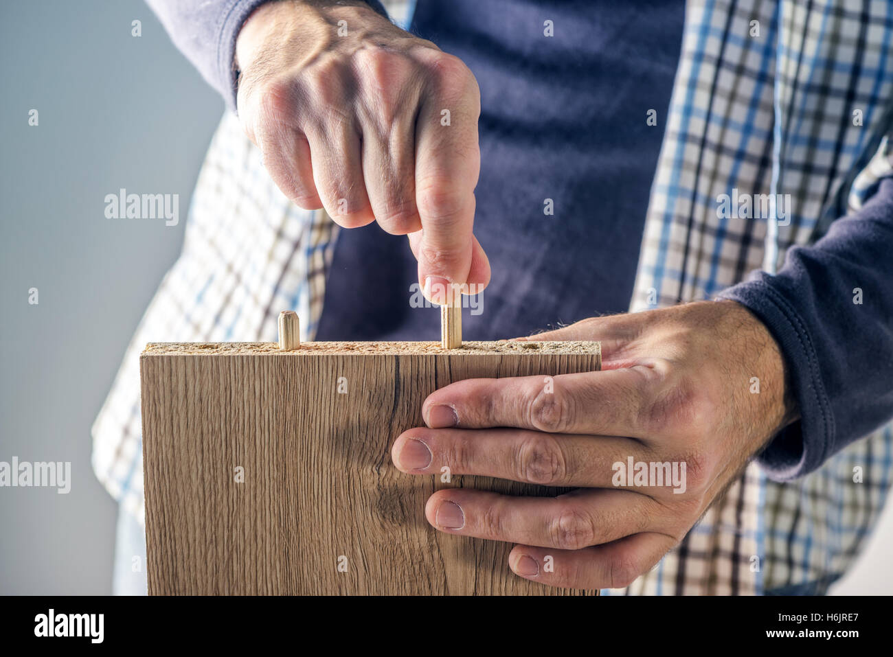 Man assembling furniture at home, male hand with wooden dowel pins and plywood board Stock Photo