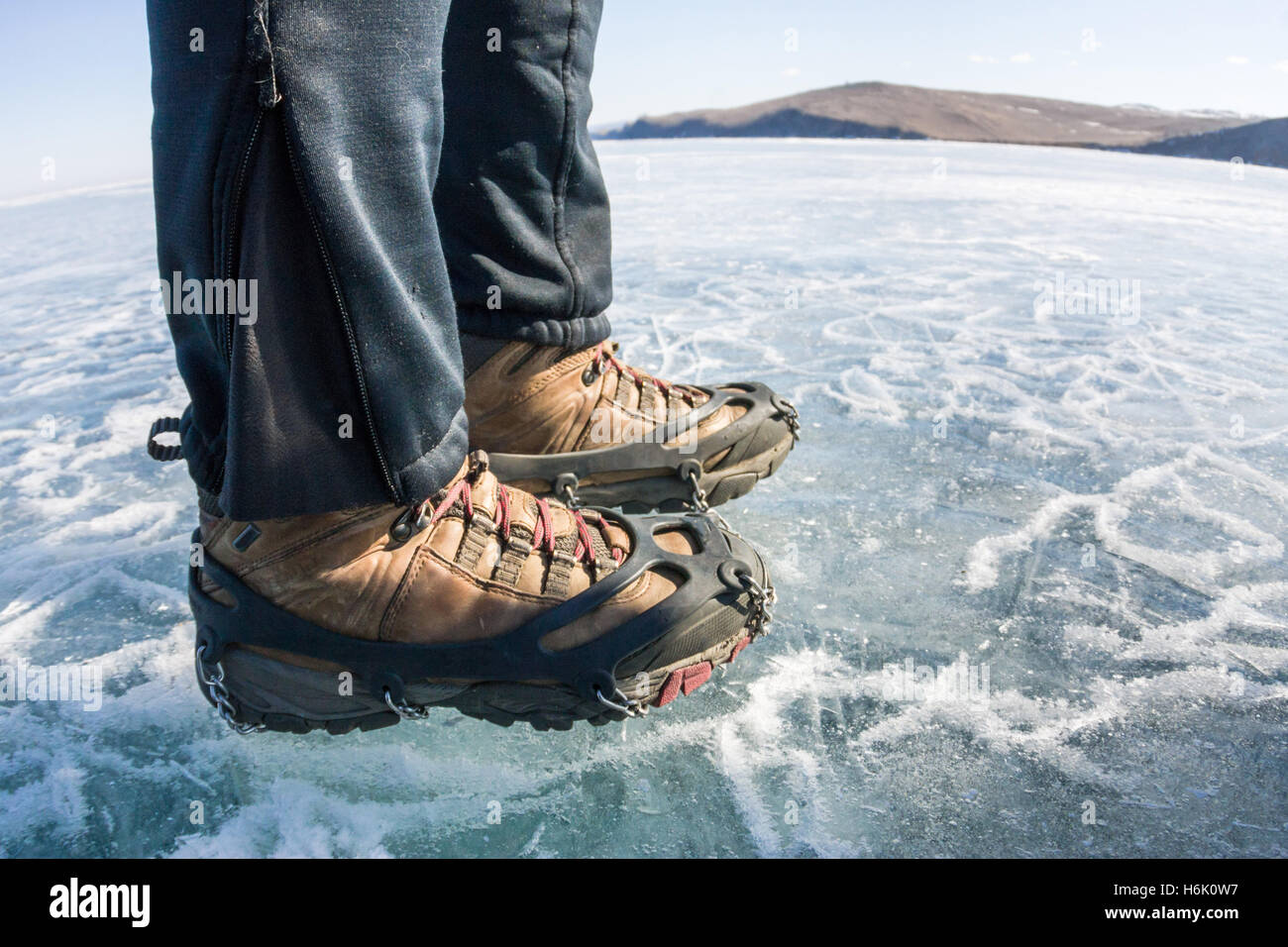 Human legs in hiking boot in ice crampons on the texture Baikal ice