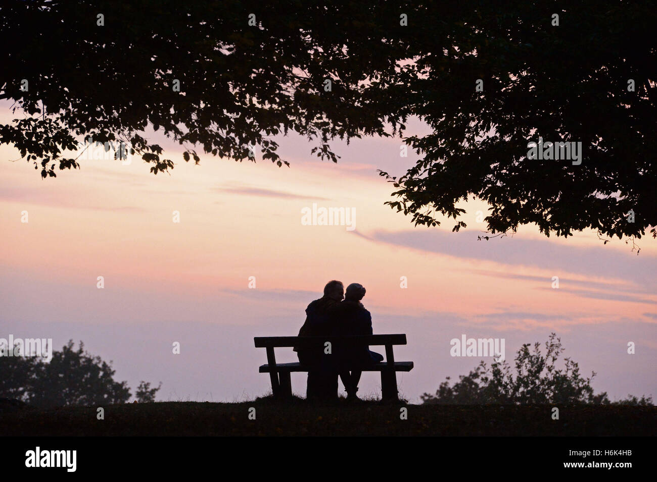 A couple sit on a bench as the sun sets in Richmond Park, London Stock ...