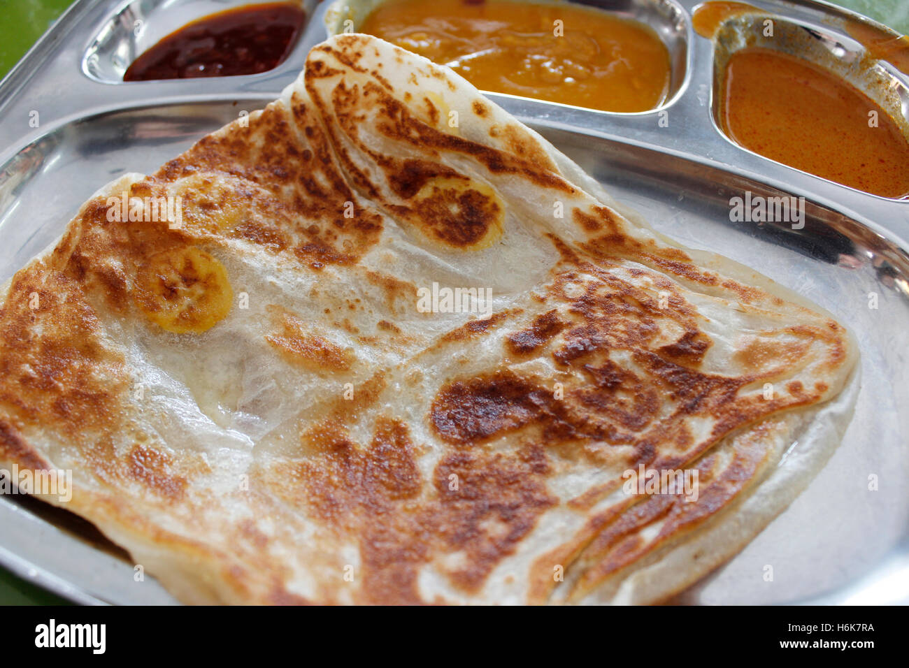 Roti canai or pan fried flatbread consisting of dough, egg, ghee and banana with the three accompanying sauces Stock Photo