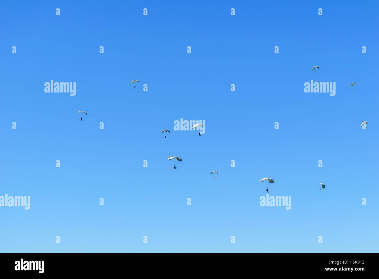 Paratroopers descend to earth on the blue clear sky background. Stock Photo
