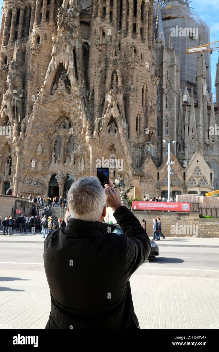 A man uses a mobile phone to take a photograph outside the Sagrada Familia entrance, Barcelona, Spain Stock Photo