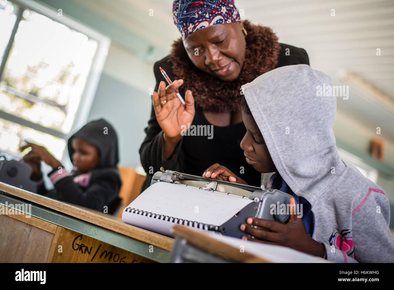 A teacher Esther Washinana helps the visually impaired learner to use Braille typewriter during