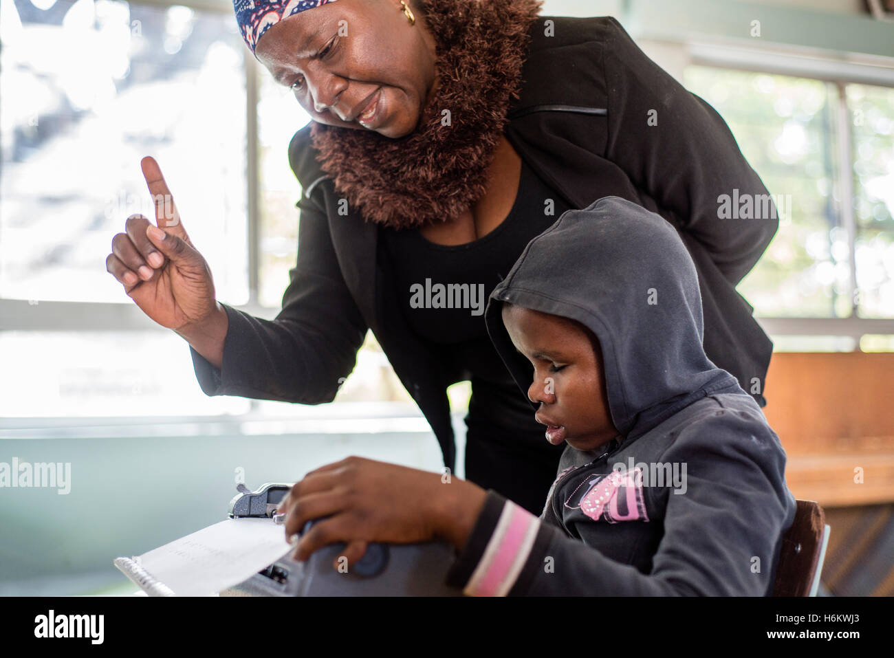 A teacher Esther Washinana helps the visually impaired learner to use Braille typewriter during