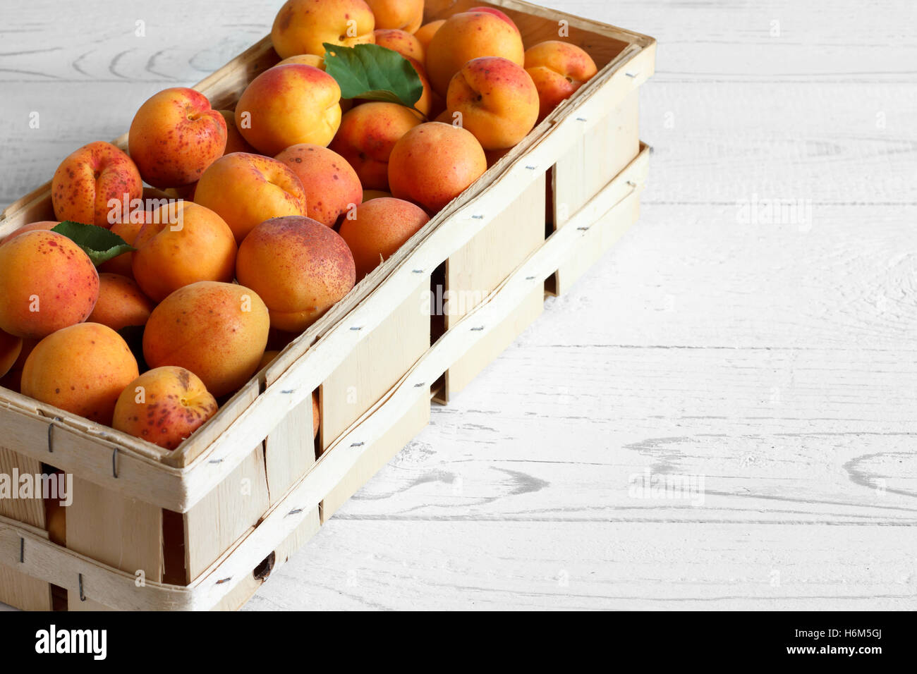 Wood box of whole orange apricots with red blush on rustic white wood ...