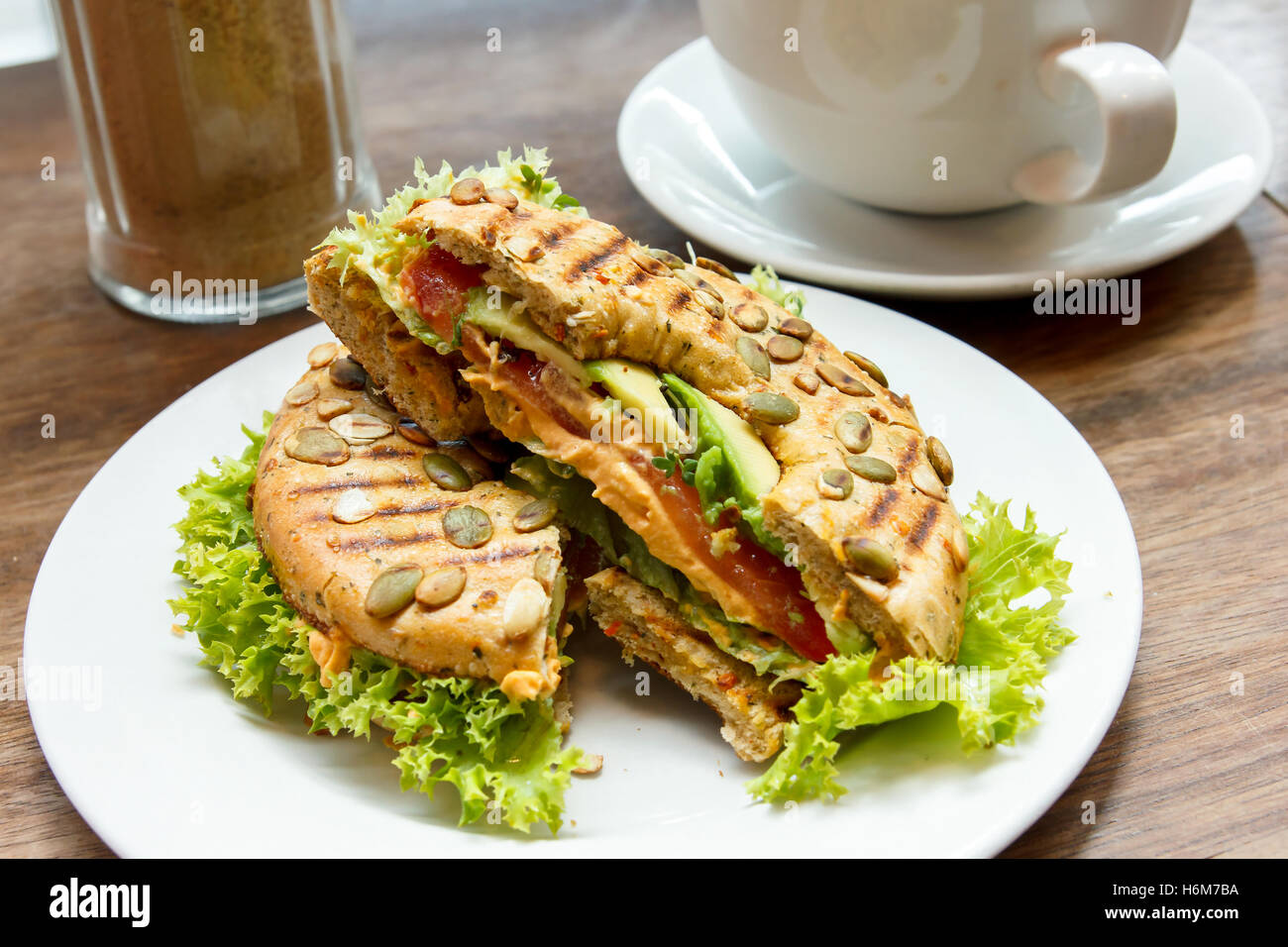 Toasted filled bagel with salad on a white plate in a cafe. Stock Photo