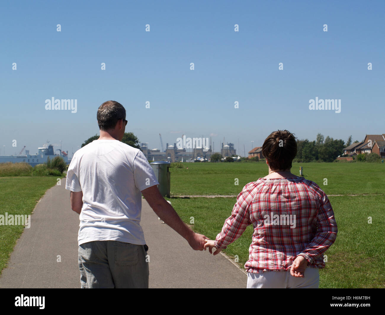 Middle aged couple walking hand in hand along Weston Shore seafront towards Woolston, Southampton, Hampshire UK Stock Photo