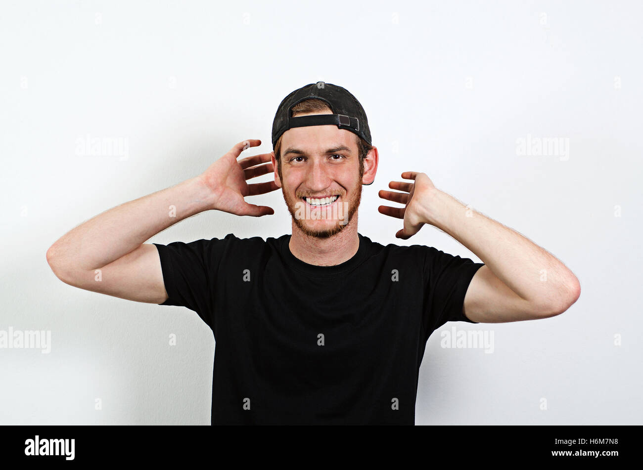Joyful and Smiling Happy Young Adult Male in Dark T-Shirt and Baseball Hat Worn Backwards Stock Photo