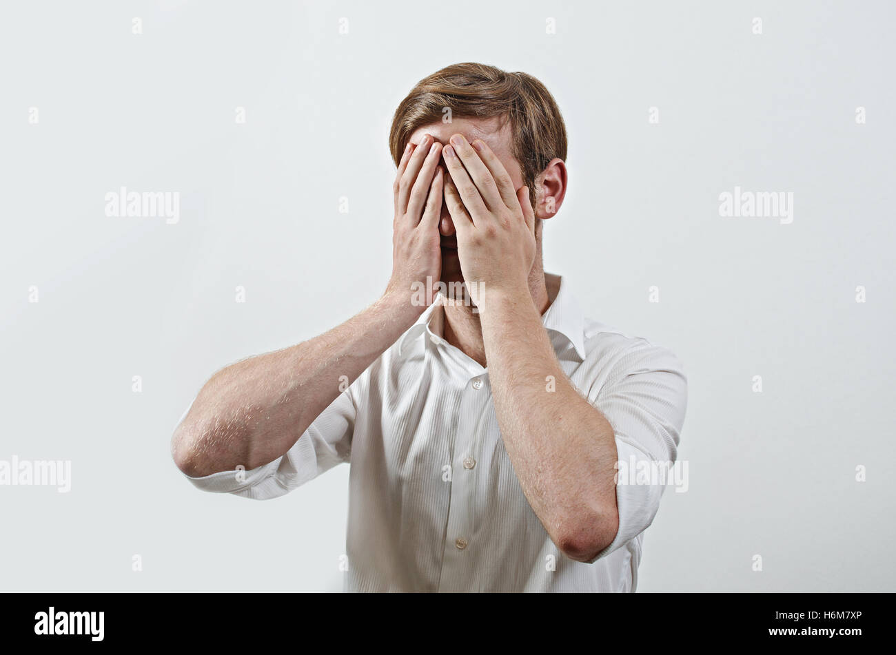 Young Adult Male Wearing White Shirt Covers His Face by Both Hands, Gesturing He Has Made a Big Mistake Stock Photo
