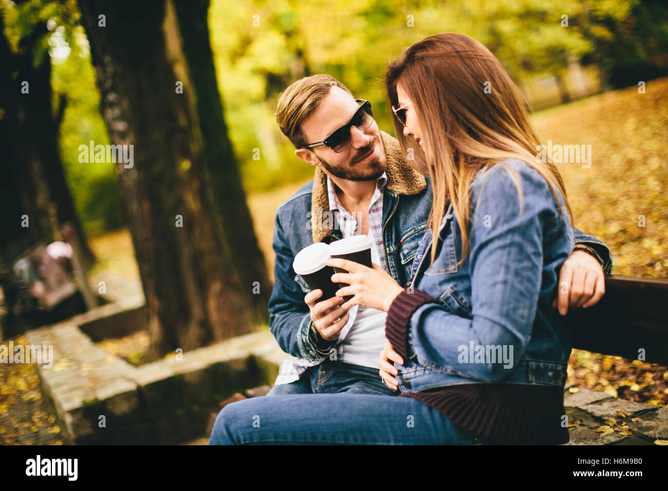 Young loving couple on a bench in autumn park and holding coffee to go in the hands Stock Photo