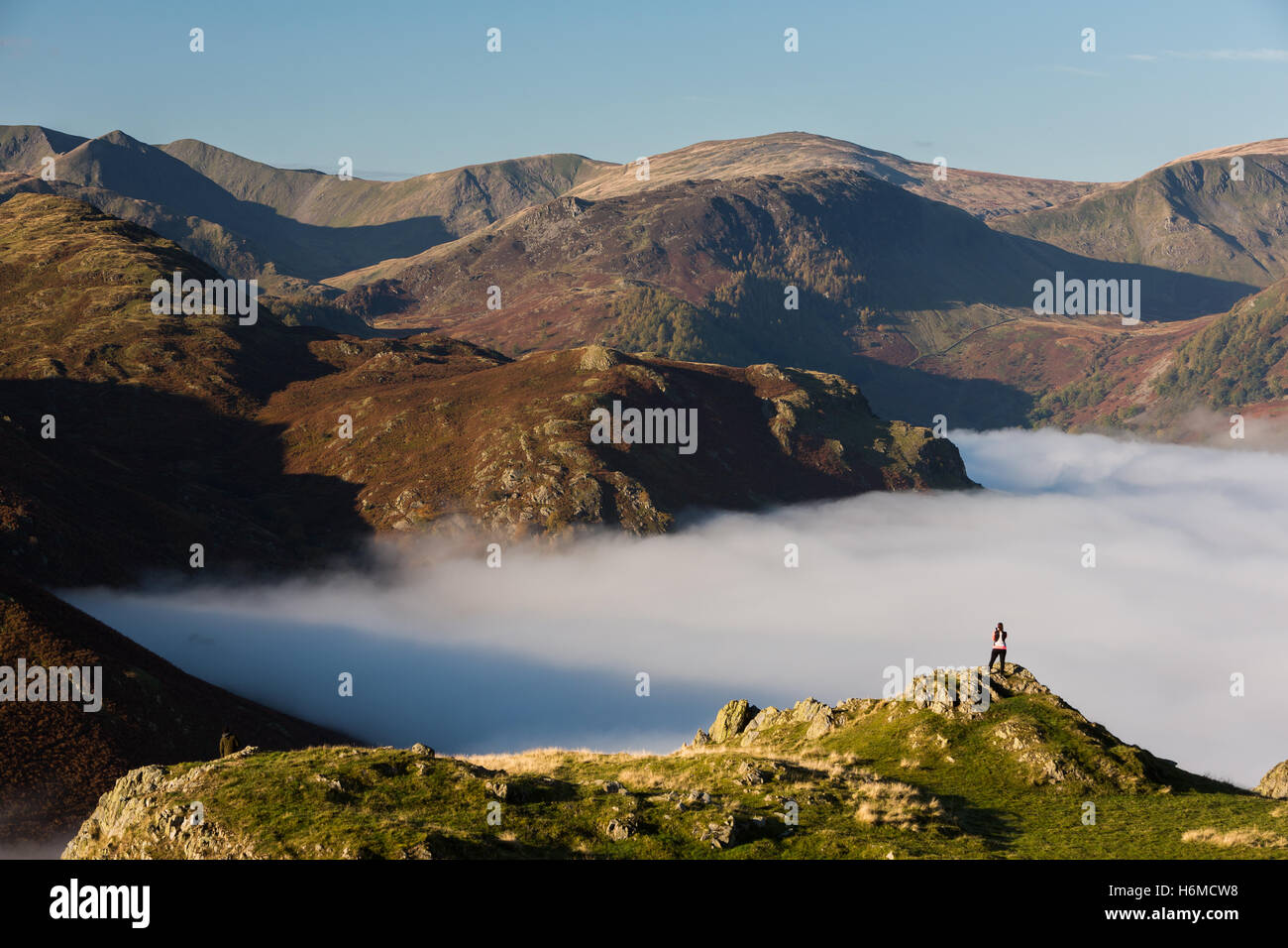 Fell runner pictured looking across the cloud inversion over Ullswater at dawn in the Lake District, England Stock Photo