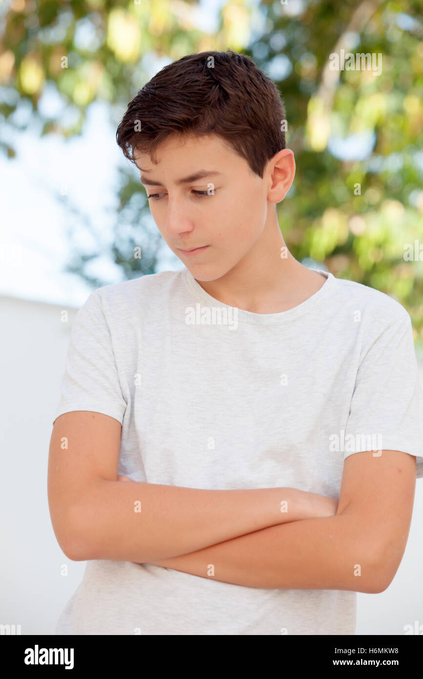 Sad teenager boy with crossed arms looking down outdoor Stock Photo