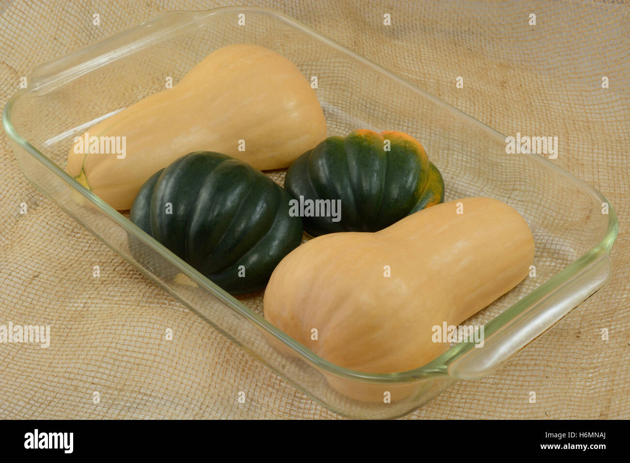 Raw uncooked acorn squash and butternut squash halves upside down in glass baking dish Stock Photo