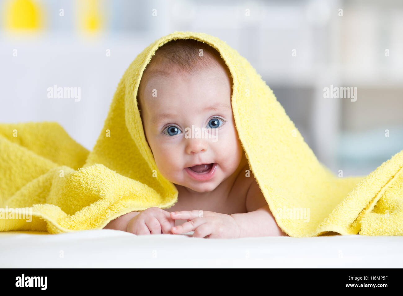 Baby girl under towel in bedroom after bath or shower. Textile and bedding for children. Stock Photo