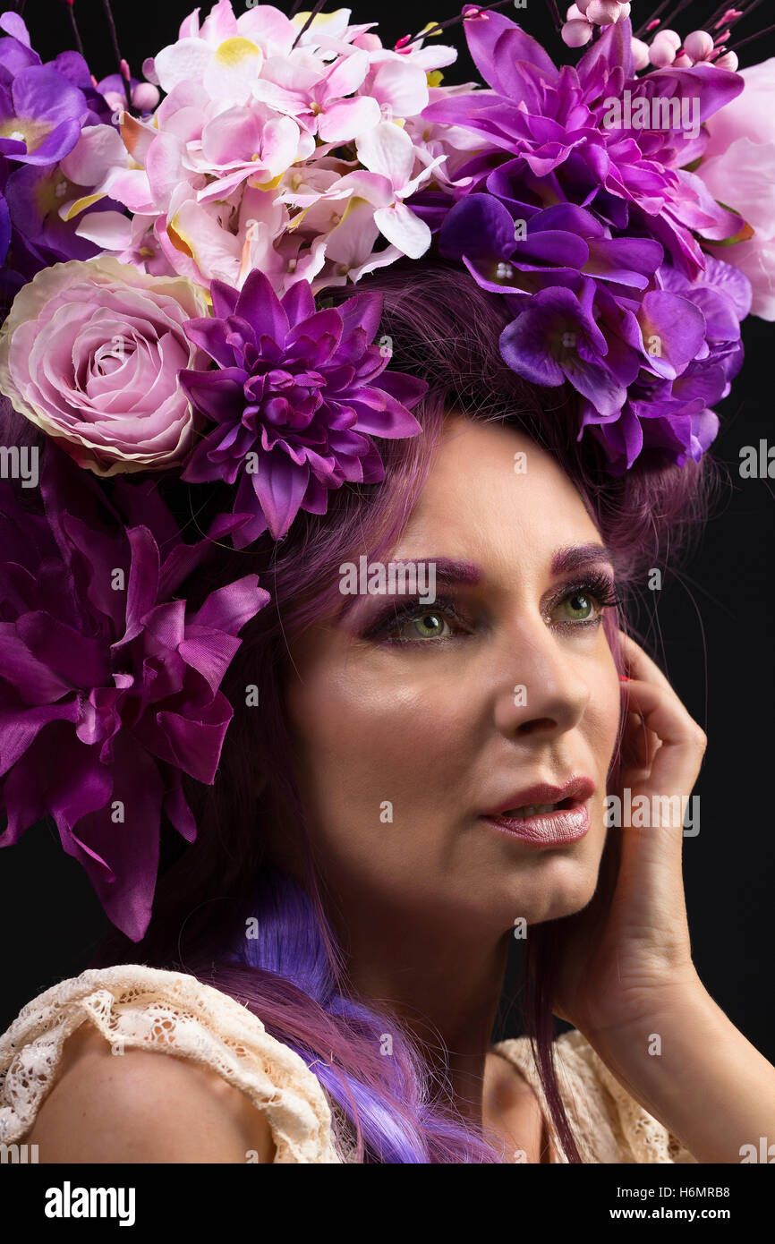 Model woman with architectural floral purple hair piece wearing white lace dress photoshoot against black studio backdrop Stock Photo