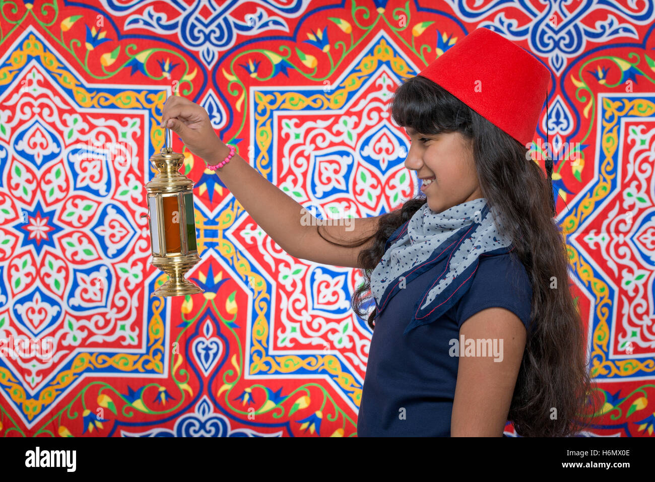 Happy Young Girl Looking at Lantern Celebrating Ramadan over Ramadan Fabric Stock Photo