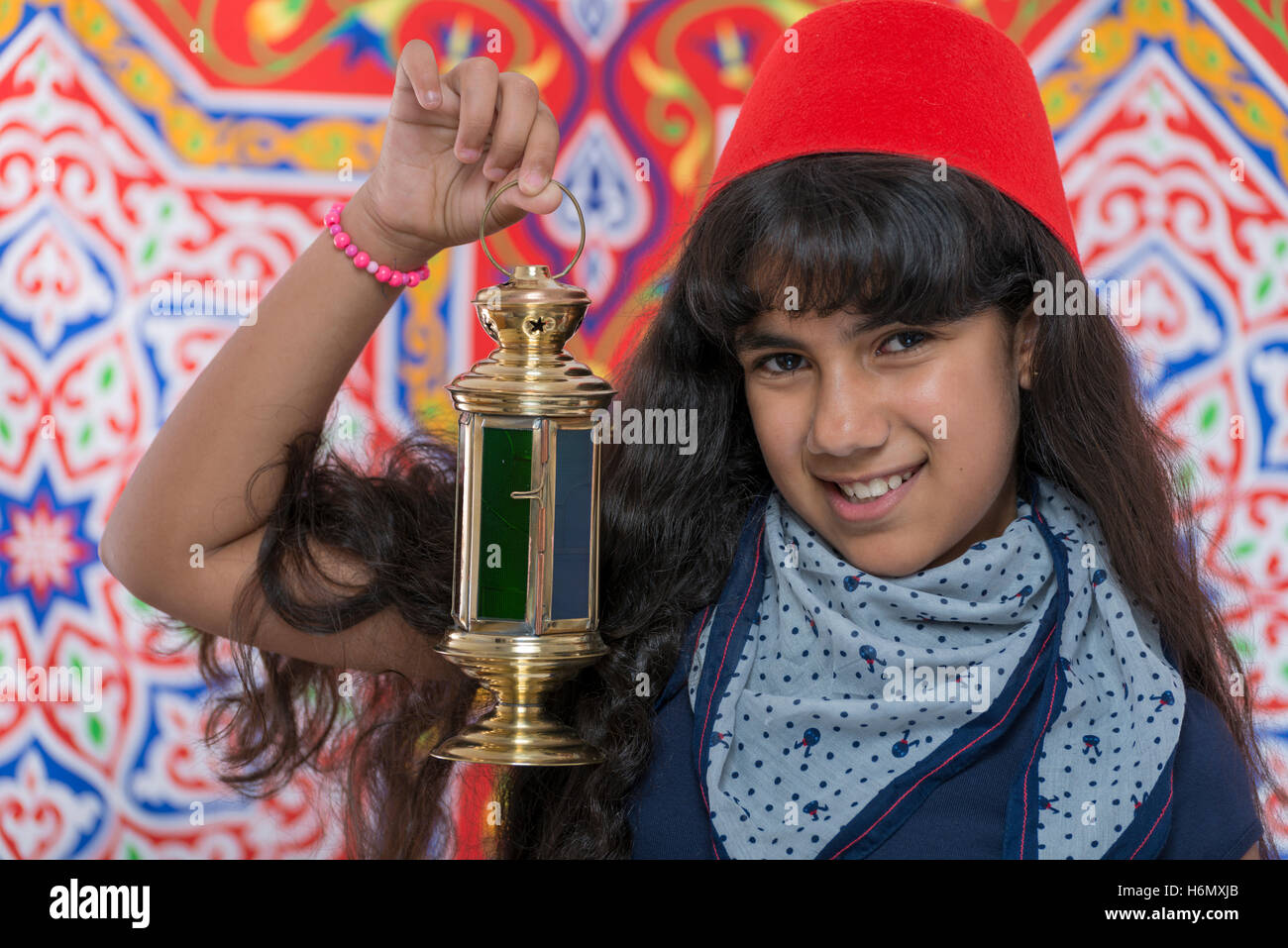 Happy Young Girl with Fez and Lantern Celebrating Ramadan over Ramadan Fabric Stock Photo