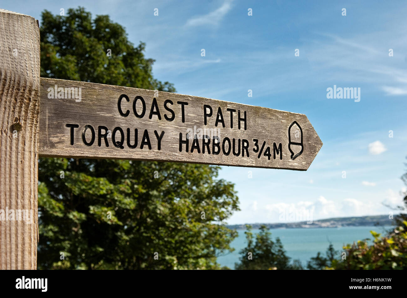 Wooden signpost points right to coast path and Torquay Harbour 3/4 mile with Tor Bay in the background on a sunny summer's day. Stock Photo