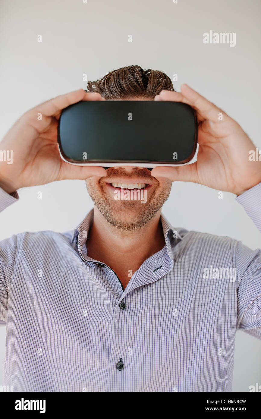 Shot of happy young man wearing virtual reality goggle against grey background. Caucasian male using VR goggle and smiling. Stock Photo