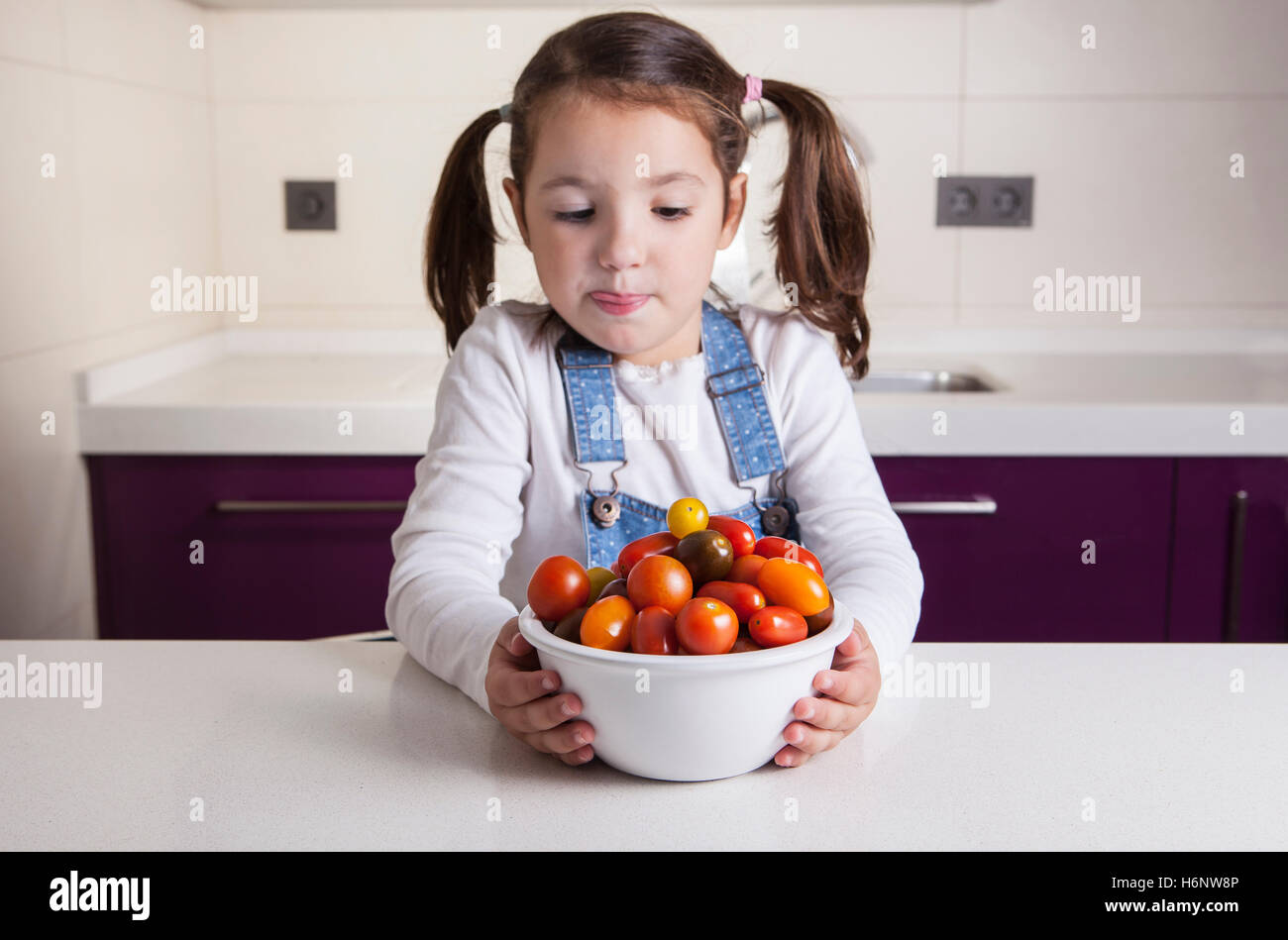Little girl licking her lips  with cherry tomatoes bowl. Education on healthy nutrition for children Stock Photo
