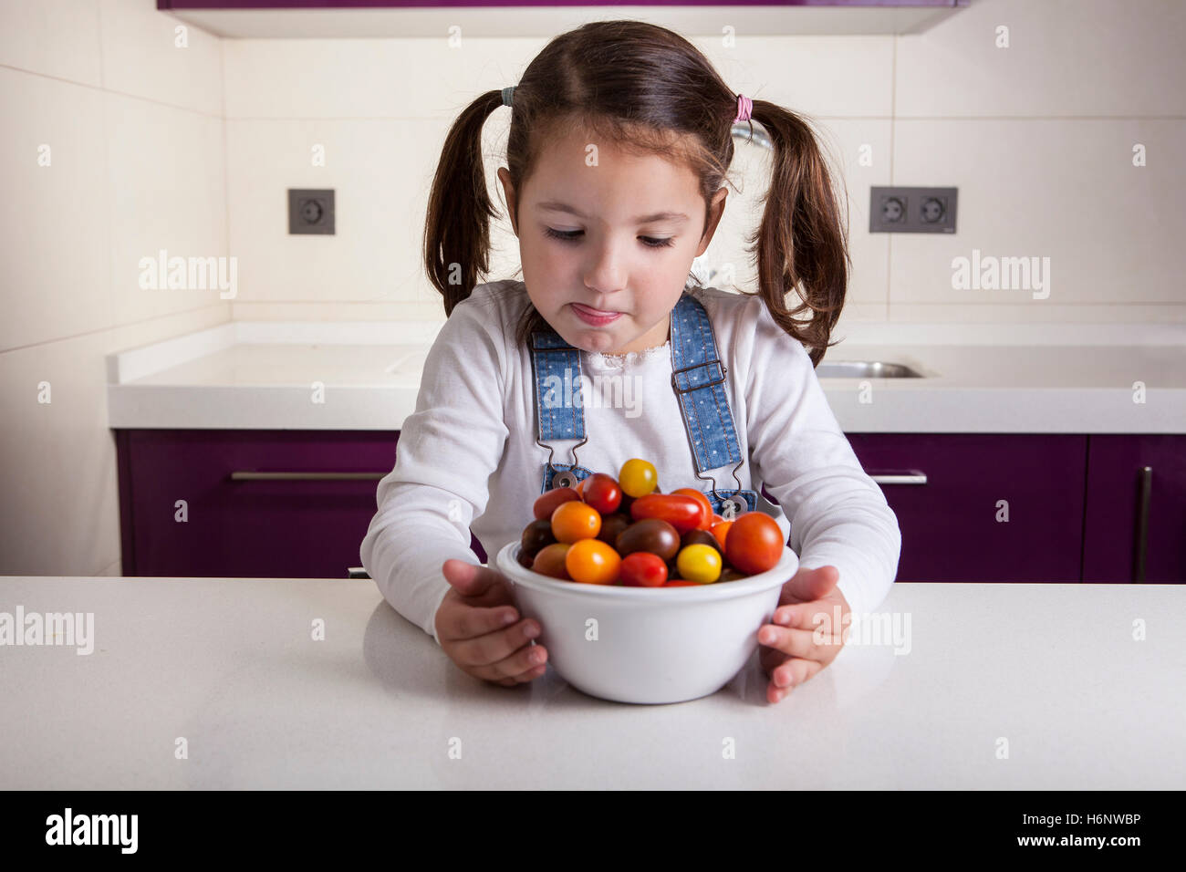 Little girl licking her lips  with cherry tomatoes bowl. Education on healthy  nutrition for children Stock Photo