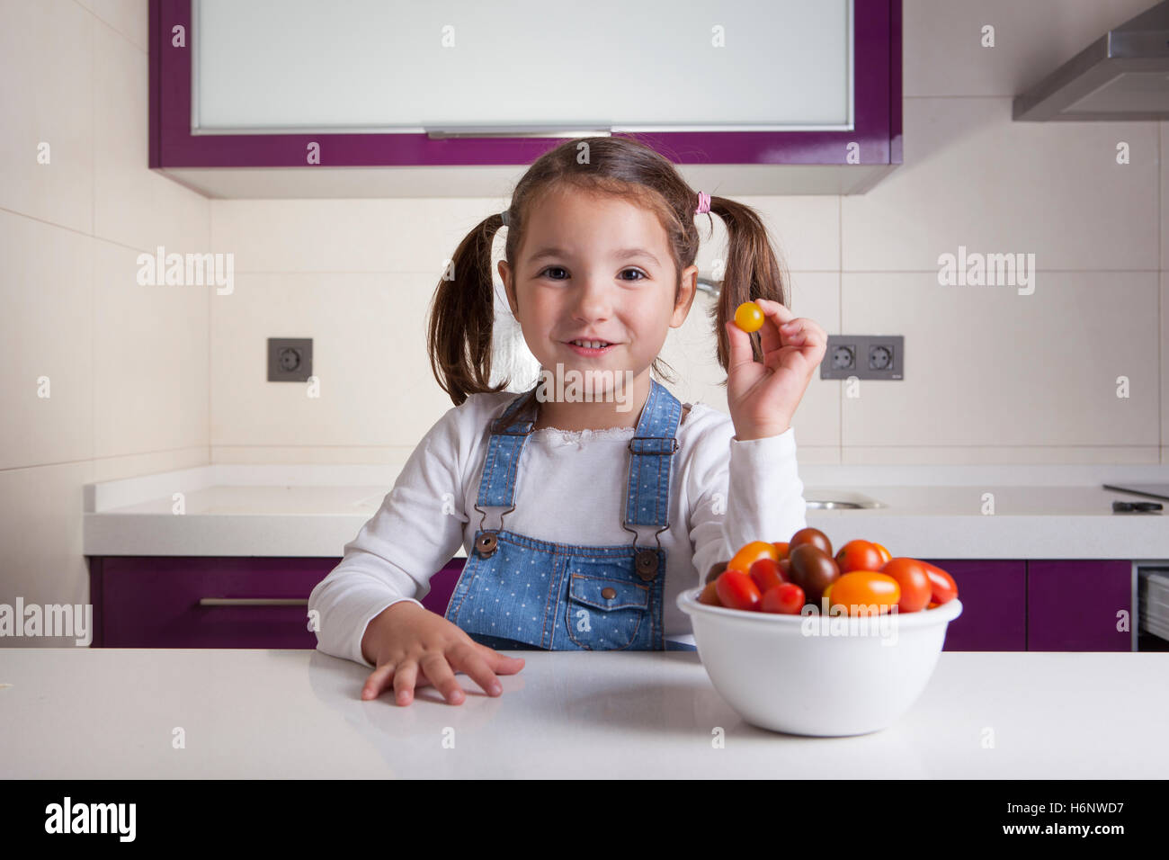 Little girl with yellow round cherry tomato in her hand. Education on healthy  nutrition for children Stock Photo