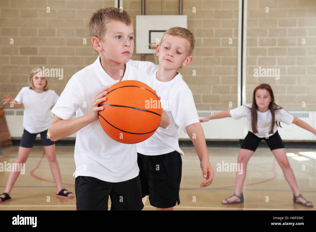 Elementary School Pupils Playing Basketball In Gym Stock Photo