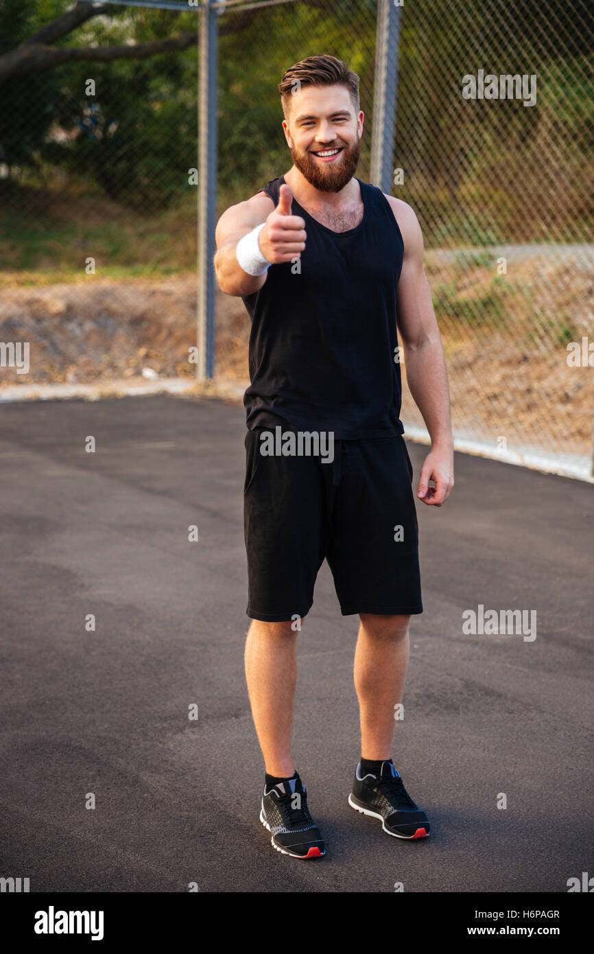 Full length portrait of a happy bearded fitness man showing thumb up outdoors Stock Photo
