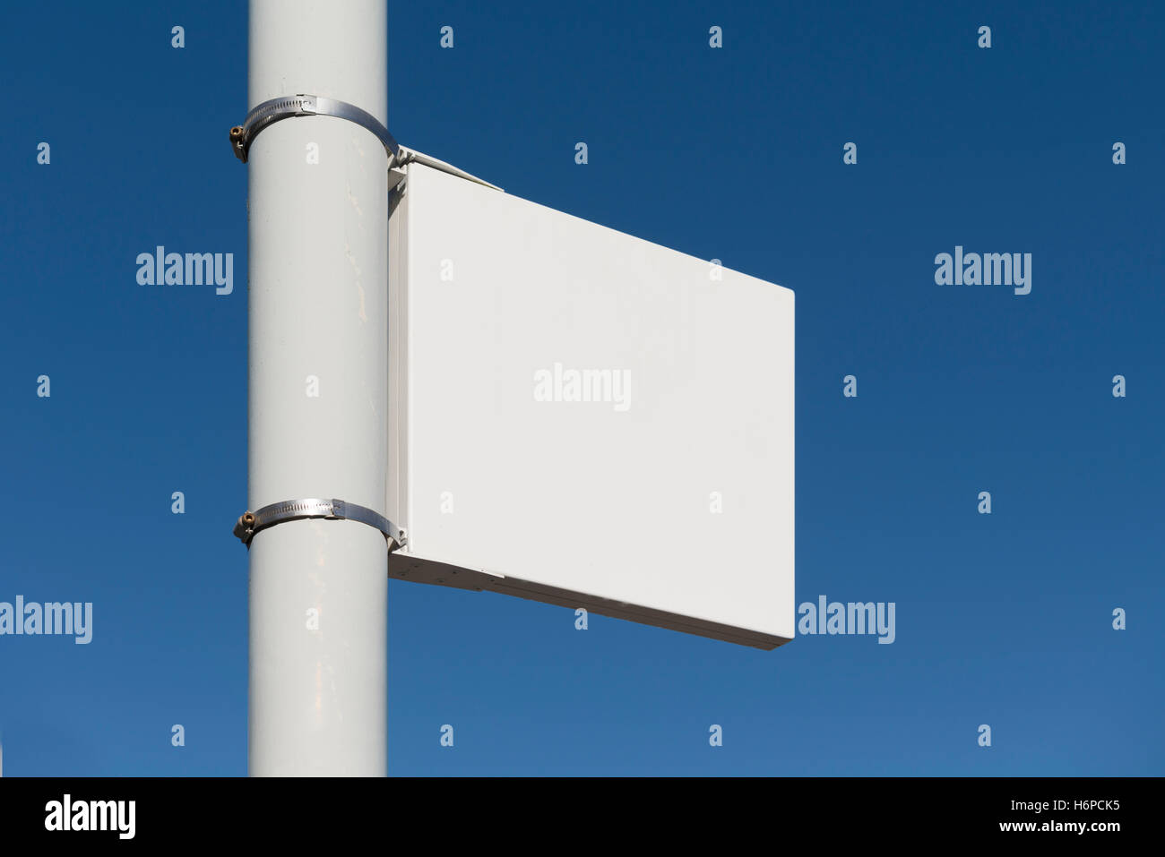 Composite image of blank white sign on grey pole against a clear blue sky on a sunny summer's day. Stock Photo
