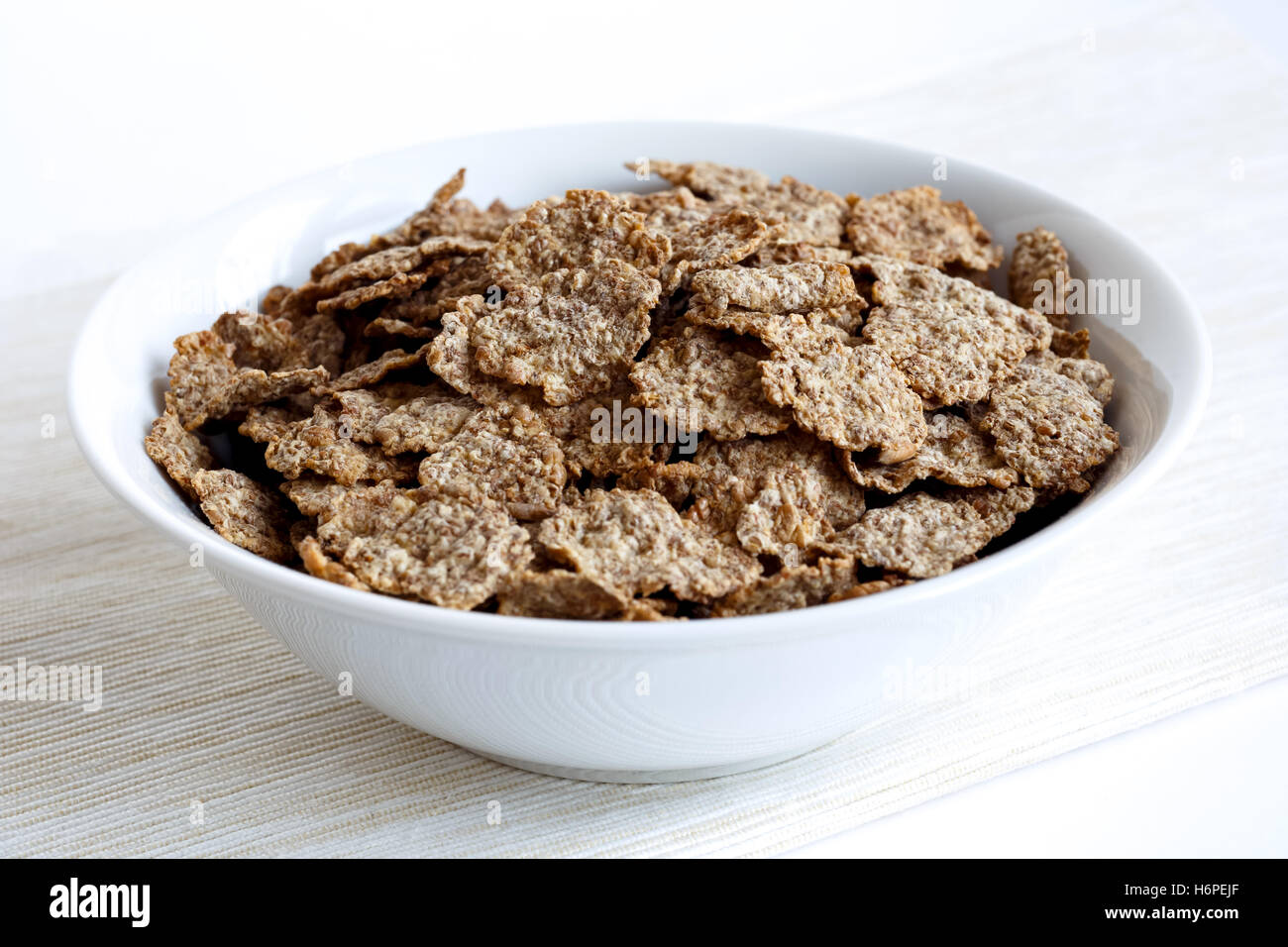 Wheat bran breakfast cereal with no milk in a bowl. On natural beige coloured textured napkin. On white background. Stock Photo