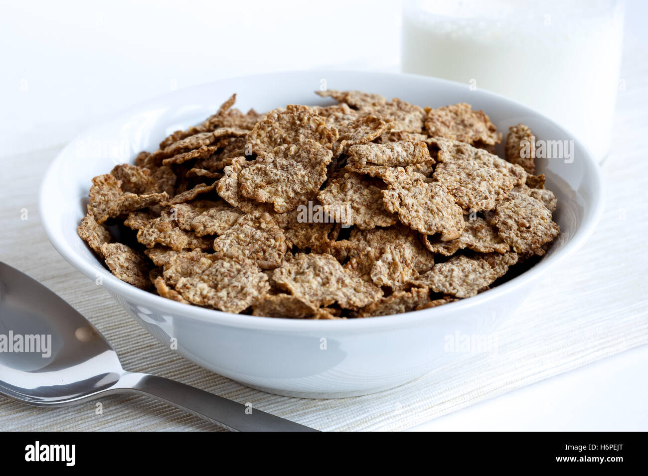 Wheat bran breakfast cereal with no milk in a bowl. On natural beige coloured textured napkin. On white background. With spoon a Stock Photo