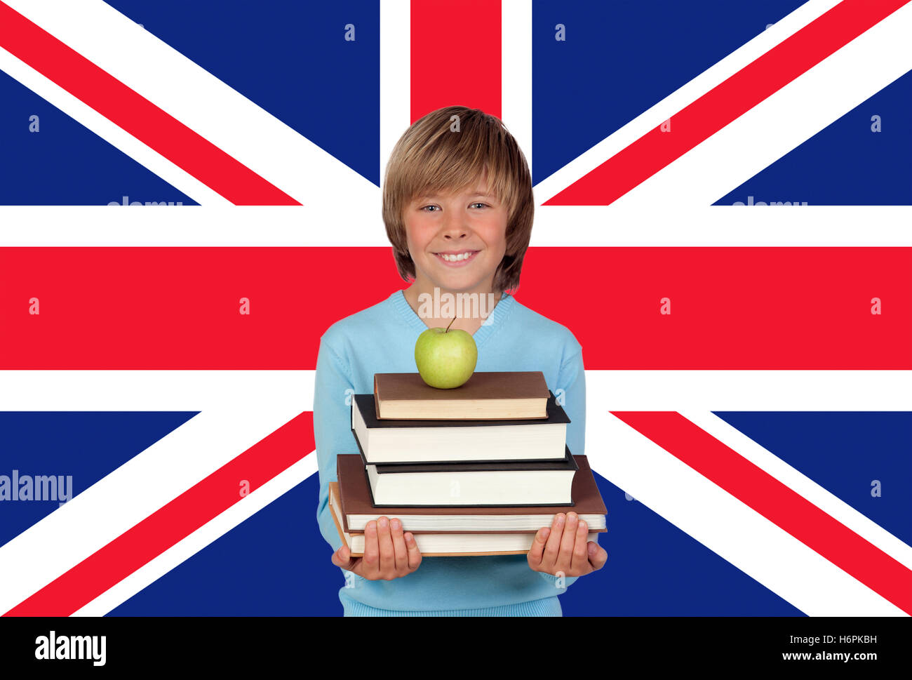 Happy Boy Holding Stack Of Books With Apple Against British Flag Stock Photo