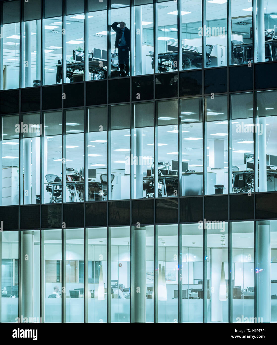 Man alone in office looking out of window at night: Coronavirus, working from home workplace stress, mental health, gig economy, loneliness...concept. Stock Photo