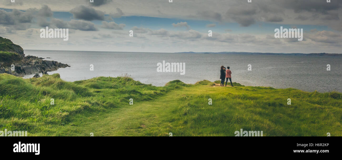 3 friends watch out over the ocean near the Galley Head lighthouse headland on a beautiful sunny Autumn morning in Ireland. Stock Photo