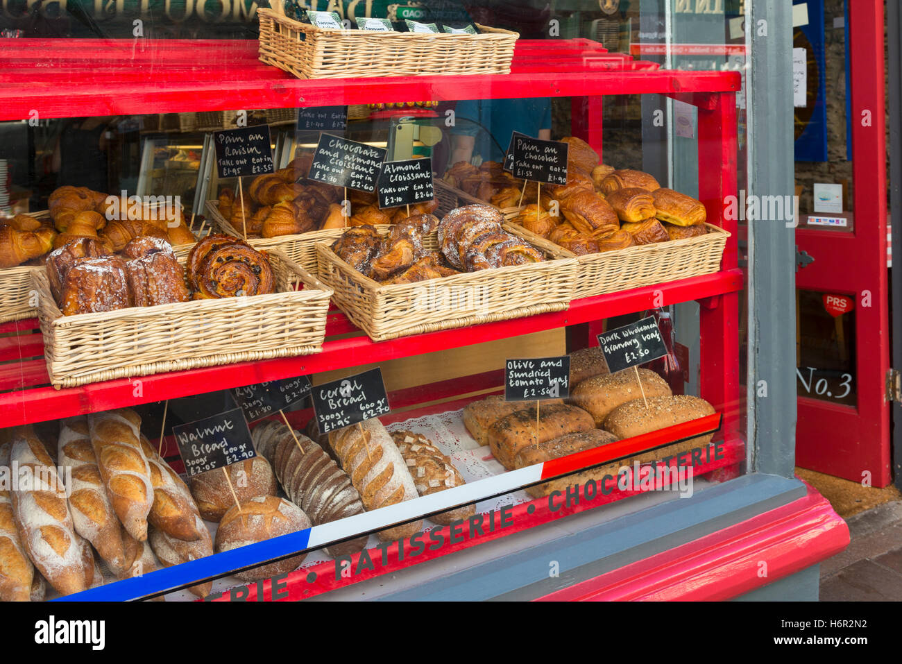 French pattiserie window display in Dartmouth showing Danish pastries artisan bread, 'pain au chocolat' croissant with prices Stock Photo