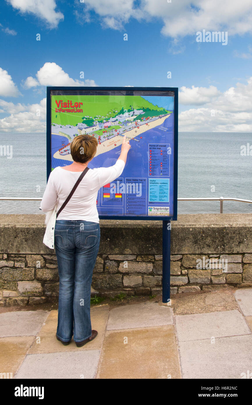 Woman tourist points at a feature on a visitor information map on promenade overlooking the sea at Teignmouth, Devon Stock Photo