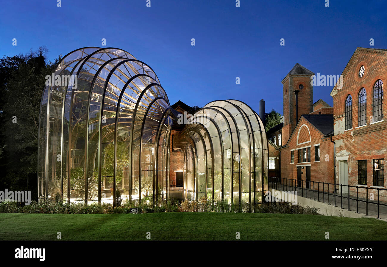 View across historic site with illuminated greenhouses. Bombay Sapphire Distillery, Laverstoke, United Kingdom. Architect: Heatherwick, 2014. Stock Photo