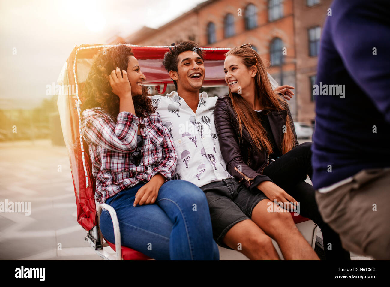 Three young friends enjoying tricycle ride in the city. Teenagers riding on tricycle on road. Stock Photo