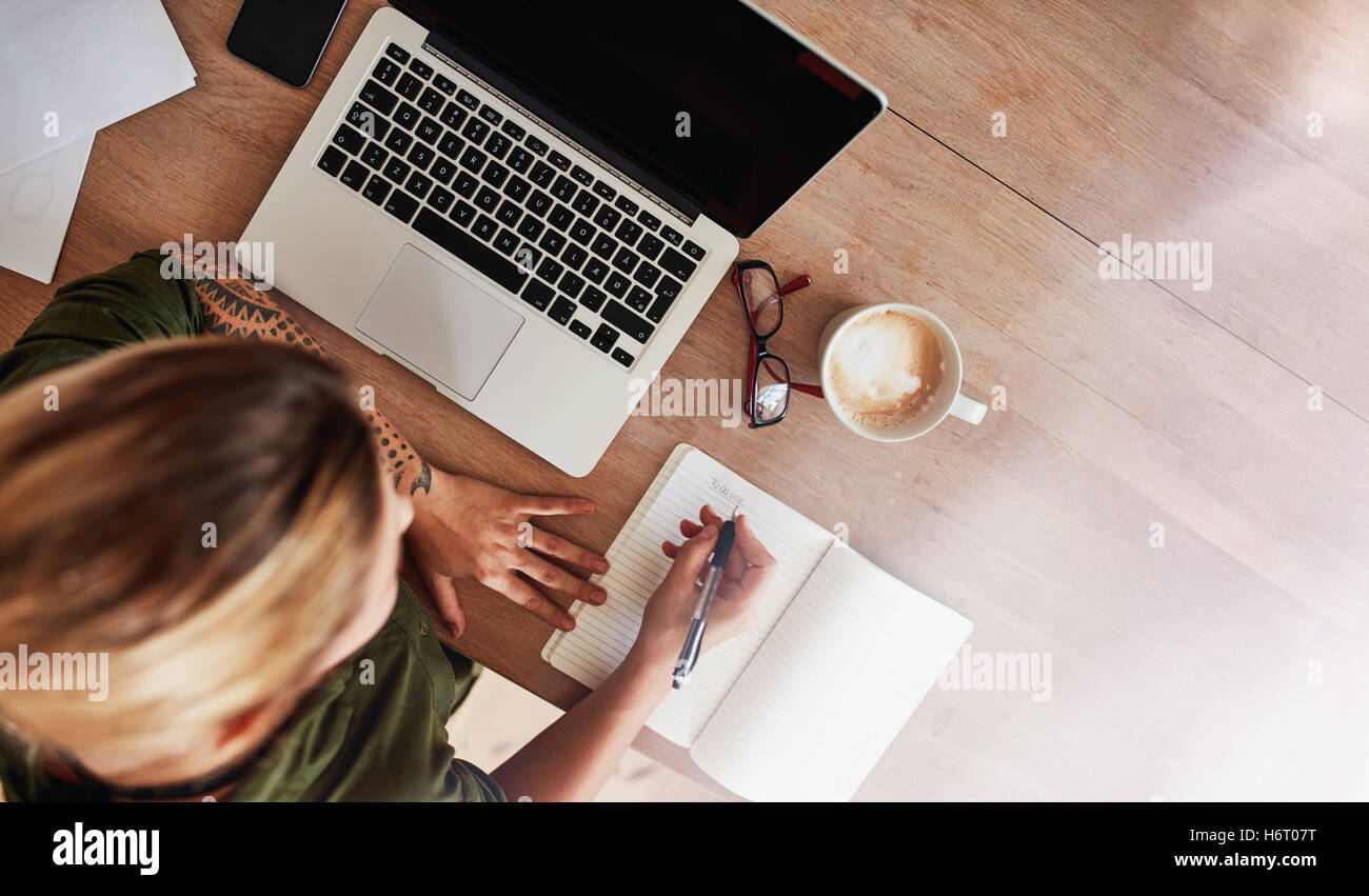 Top view shot of woman sitting at table with laptop and coffee writing on notebook. Female making to do list on diary. Stock Photo