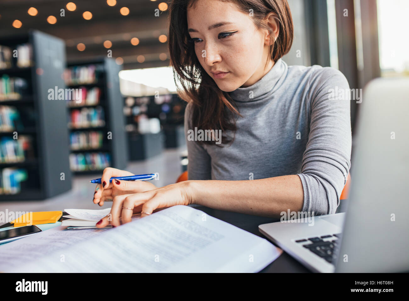 Young woman studying on a book and taking down note while sitting at the library desk. Asian female student preparing for final Stock Photo