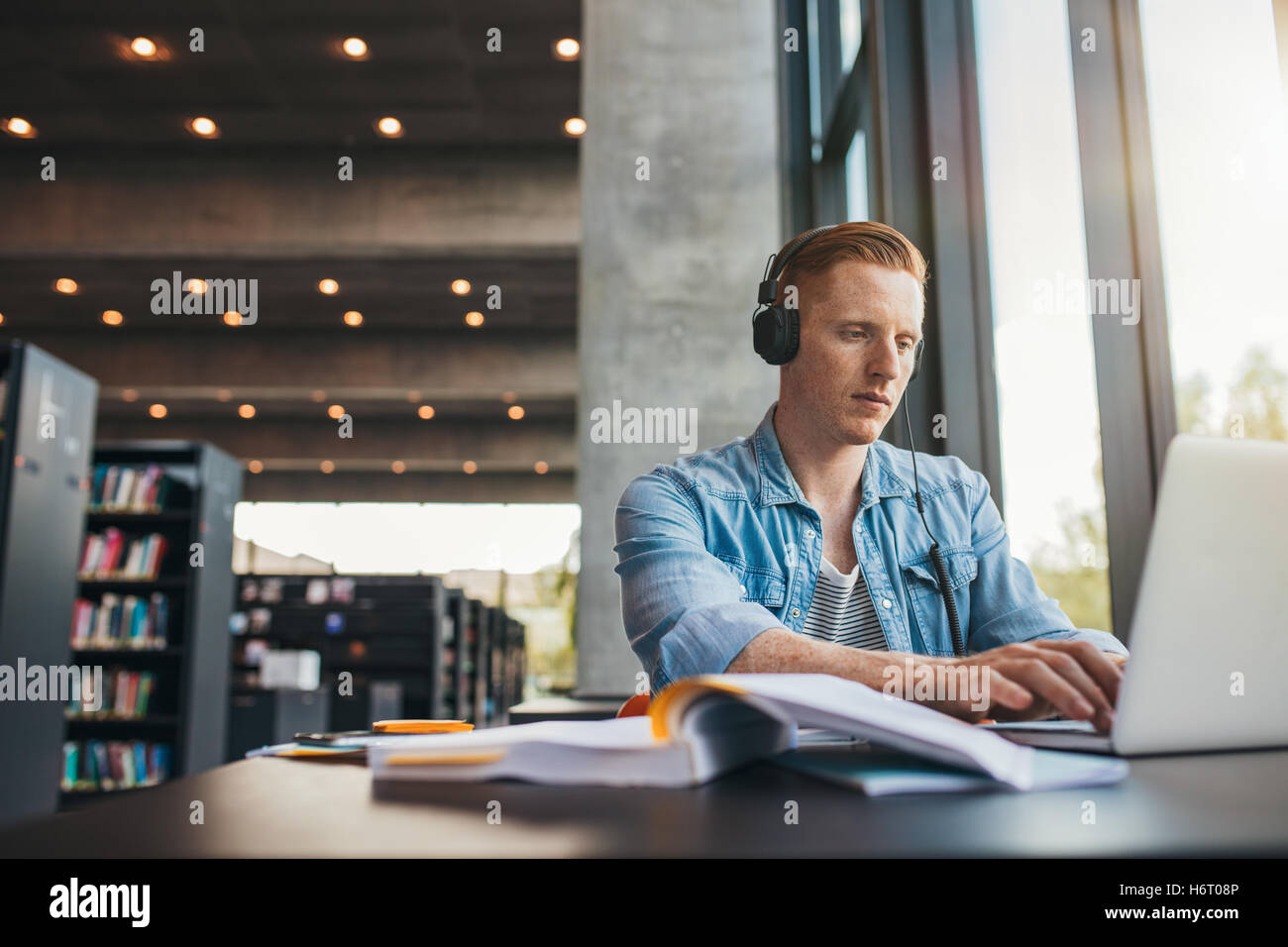 Young male student with headphones studying on the laptop. Handsome caucasian man sitting at the desk and working on laptop at p Stock Photo