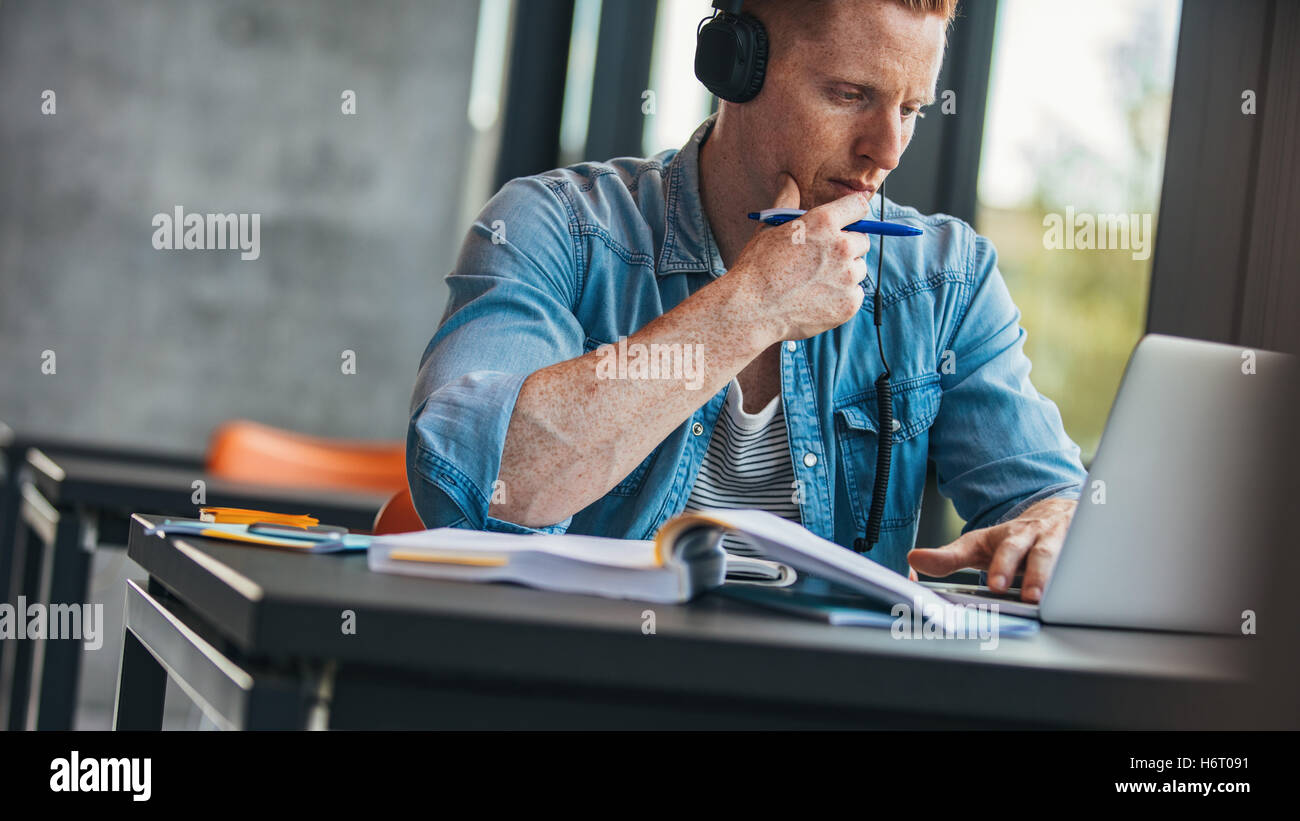 Pensive student with laptop studying in the university library. Young man using laptop and thinking. Stock Photo