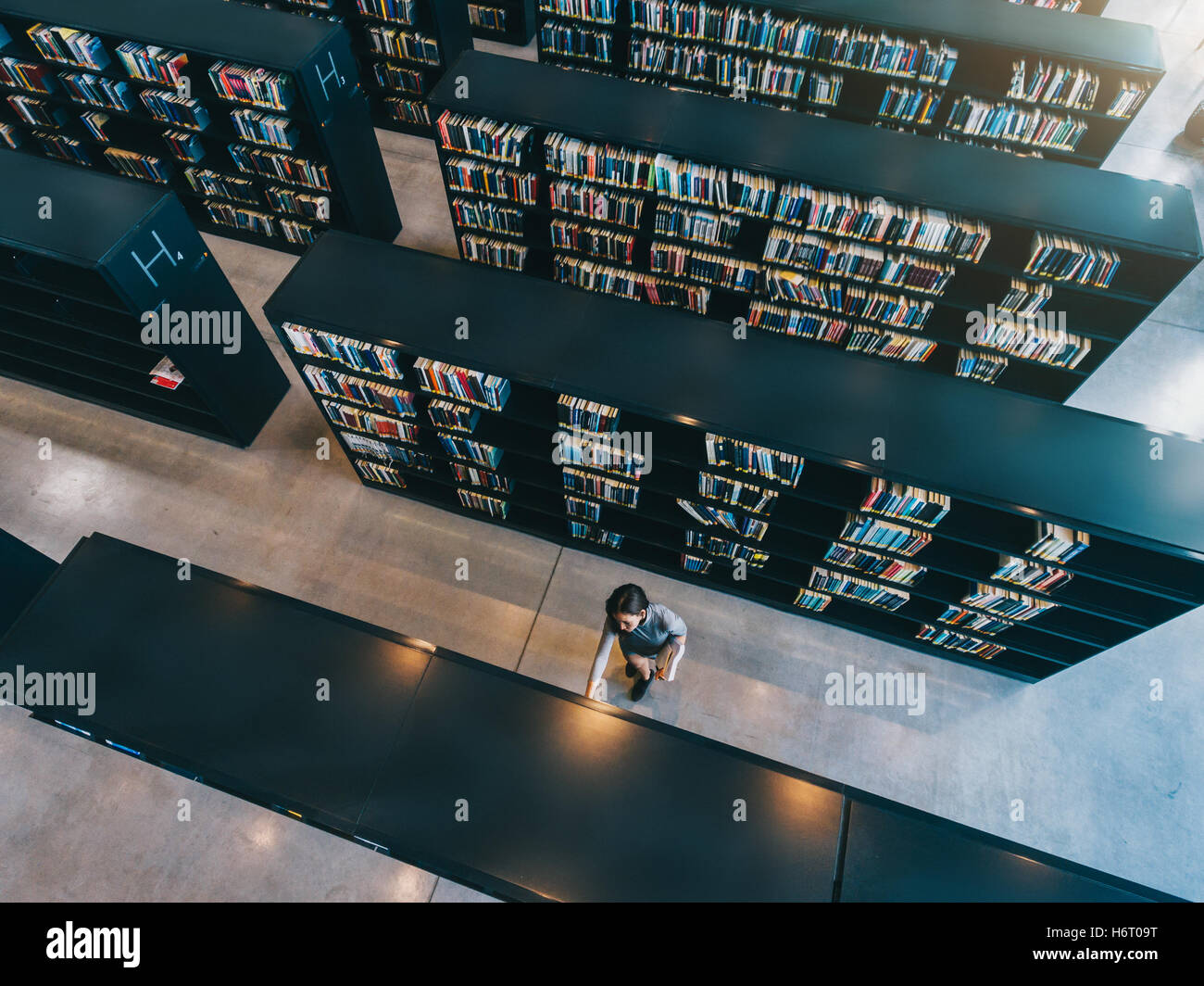 Overhead view of young woman looking for a book in shelf. university student in library selecting a book. Stock Photo